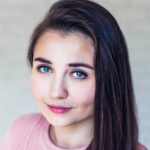 Portret kobiety z długimi, brązowymi włosami i niebieskimi oczami, ubranej w różowy sweter.