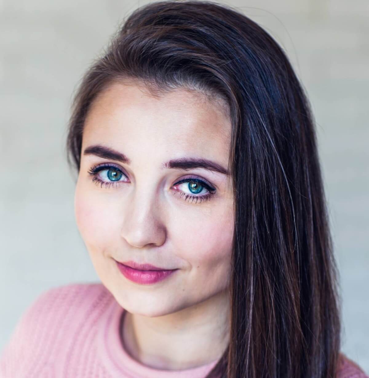 Portret kobiety z długimi, brązowymi włosami i niebieskimi oczami, ubranej w różowy sweter.