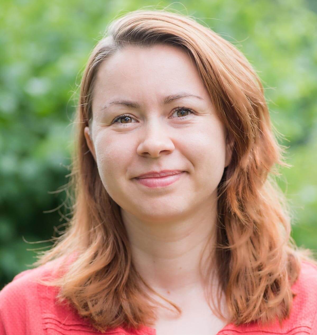 Portret uśmiechniętej osoby w czerwonoróżowym swetrze na tle zieleni.