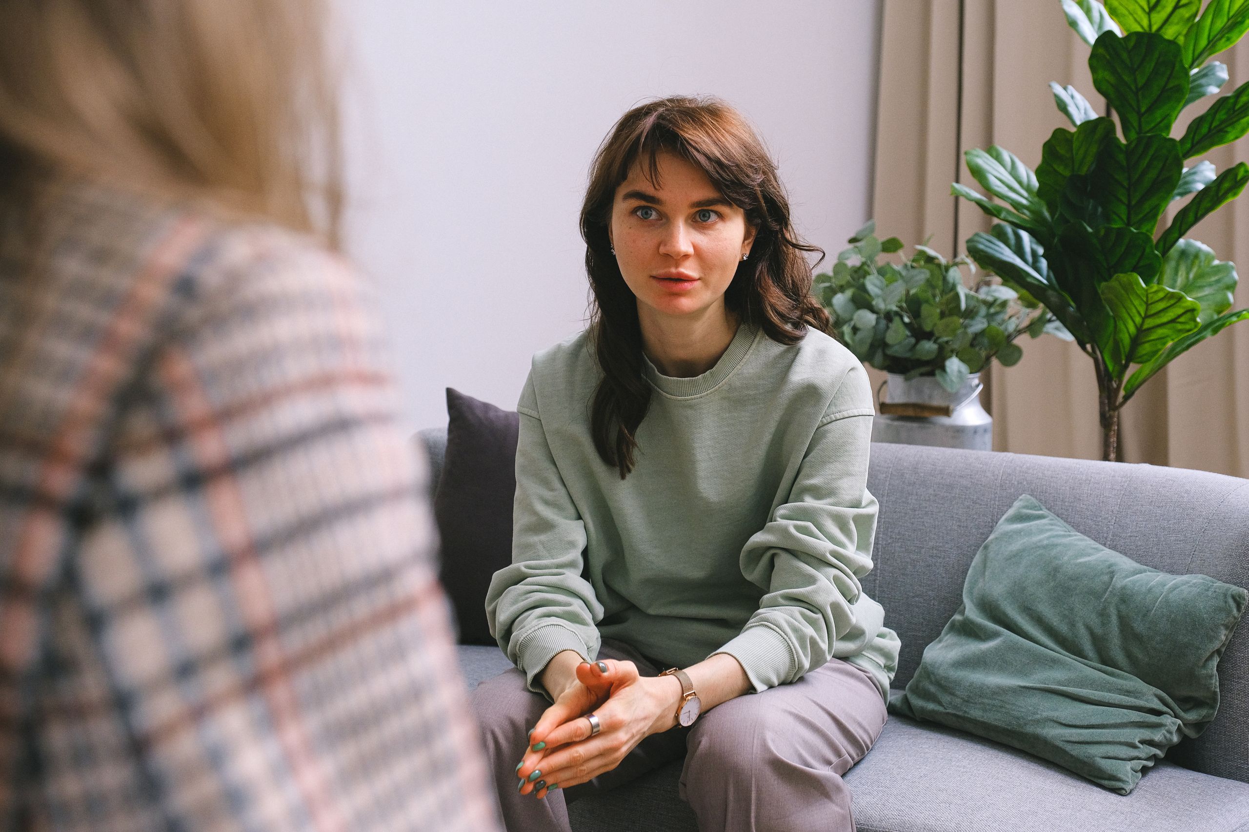 Female in casual clothes sitting on sofa and looking at crop therapist during session in cozy office