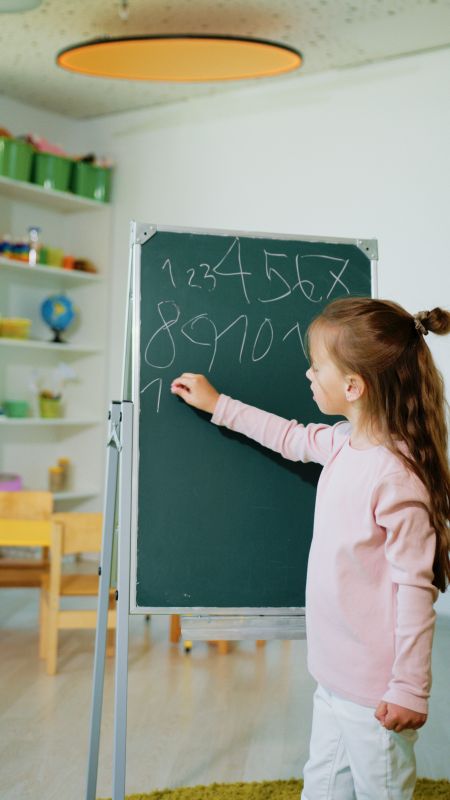 Dziewczynka pisze liczby na zielonej tablicy w jasnej sali lekcyjnej.